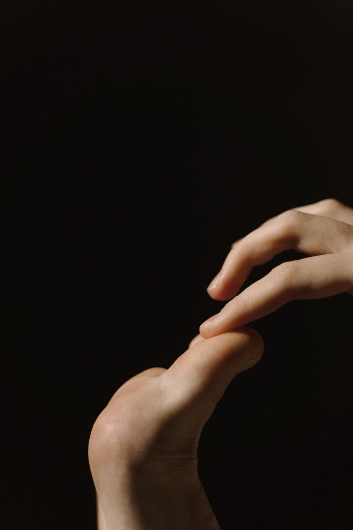 Artistic close-up of human hands touching toes against a dark backdrop.